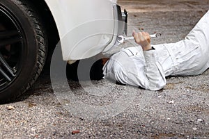Professional mechanic in white uniform lying down and fixing under car. Auto repair service.