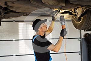 Professional mechanic is working on a car in a car service. Auto mechanic man in blue overalls with lamp working at