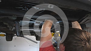 Professional mechanic working underneath a lifting vehicle at auto service. Repairman in uniform inspecting bottom of a