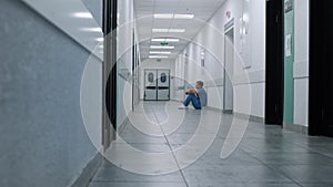 Professional medic resting alone in hospital corridor. Surgeon sitting on floor.