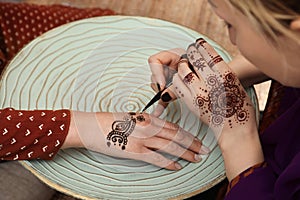 Professional mehndi master making henna tattoo at table