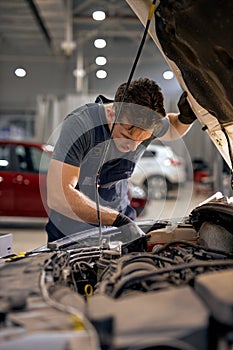 professional Mid adult mechanic repairing system of car in hood in auto repair shop.