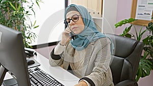 Professional middle-aged woman in hijab speaking on phone in modern office setting photo