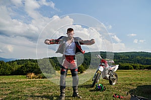 A professional motocross rider, clad in a full suit, gloves, and backpack, prepares for a daring adventure through the