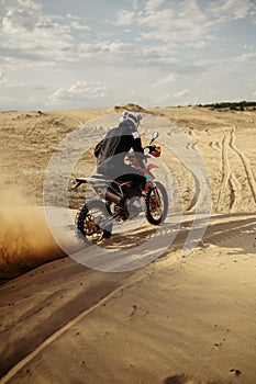 Professional motocross rider driving on sand dune