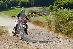 A professional motocross rider exhilaratingly riding a treacherous off-road forest trail on their motorcycle.