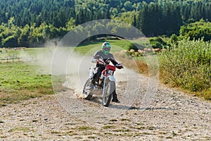 A professional motocross rider exhilaratingly riding a treacherous off-road forest trail on their motorcycle.