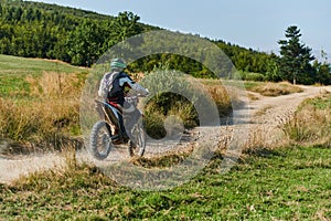 A professional motocross rider exhilaratingly riding a treacherous off-road forest trail on their motorcycle.