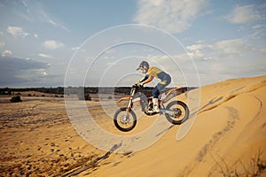 Professional motocross rider sliding down sand hill