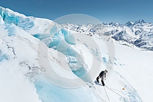 A professional mountaineer in a helmet and ski mask on insurance makes a nick-hole in the glacier against the backdrop