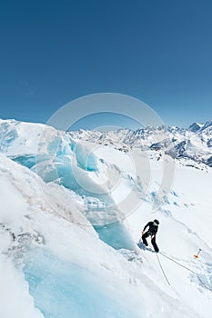 A professional mountaineer in a helmet and ski mask on insurance makes a nick-hole in the glacier against the backdrop