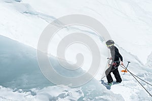 A professional mountaineer in a helmet and ski mask on insurance makes a nick-hole in the glacier against the backdrop