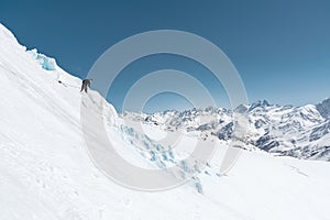 A professional mountaineer in a helmet and ski mask on insurance makes a nick-hole in the glacier against the backdrop