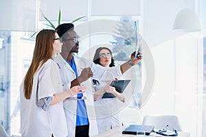 Professional multi ethnic doctors are examining a patient`s X-ray. Two female doctors and one male doctor work together