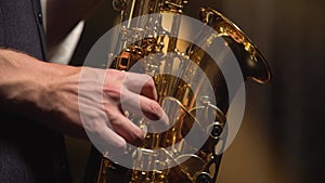 Professional musician fingering keys playing golden shiny saxophone on stage. Dark studio with smoke and neon lighting