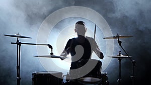 Professional musician plays music on drums with the help of sticks. Smoky background. Silhouette