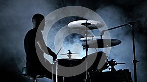 Professional musician plays music on drums . Smoky background. Side view. Silhouette. Back light. Slow motion
