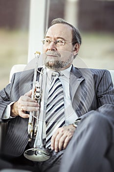 Portrait of a musician with a trumpet sitting in a chair, on the background of the concert hall