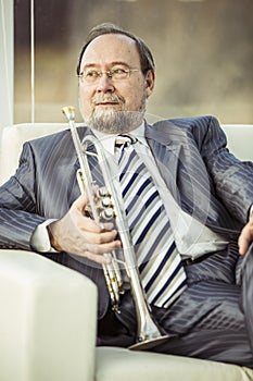 Portrait of a musician with a trumpet sitting in a chair, on the background of the concert hall
