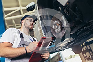 Professional near the car hanging on the lift at the service station make a diagnostics