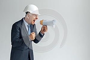 Professional Occupation. Constructor in hard hat standing isolated on gray shouting at speaker angry making fist