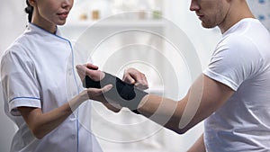 Professional orthopedist fixing wrist support pleased male patient, healthcare