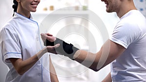Professional orthopedist fixing wrist support pleased male patient, healthcare