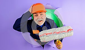 Professional painter or decorator with painting roller looking through hole in paper. Repair and building concept.