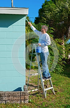 Professional painter or homeowner man on a ladder with paint can and brush painting the exterior of a residential house
