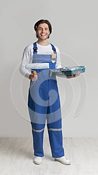 Professional Painter In Work Uniform Holding Paint Roller And Smiling At Camera