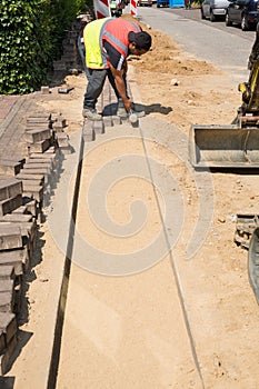 Professional paver worker placing pave stones and using a hammer.