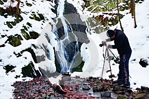 Professional photograph takes with camera on tripod photo of winter waterfall.