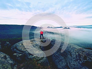 Professional photographer above clouds. Man takes photos with camera on tripod on rocky peak.