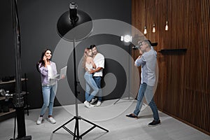 Professional photographer with assistant taking picture of young couple in studio