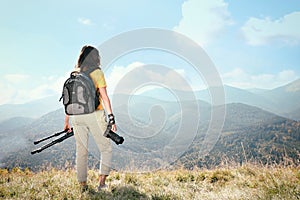 Professional photographer with modern camera and tripod in mountains, back view. Space for text