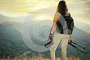Professional photographer with modern camera and tripod in mountains, back view. Space for text