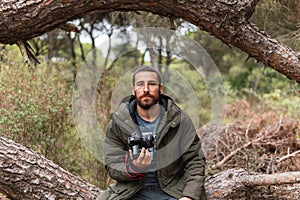 Professional photographer sitting in a tree with his camera in his hand looking straight ahead