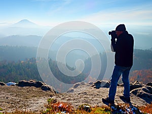 Professional photographer takes photos with mirror camera on peak of rock. Dreamy fog