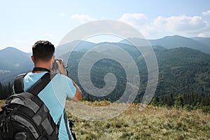 Professional photographer taking picture with modern camera in mountains, back view. Space for text