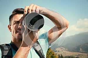 Professional photographer taking picture with modern camera in mountains, focus on lens