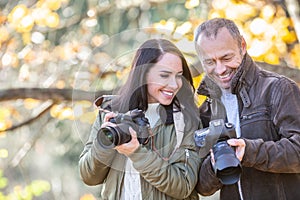 Professional photographer teaches photography to his student outdoors, both smiling at the picture in his camera