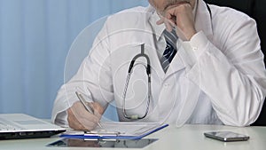 Professional physician writing treatment prescription in patient medical record