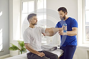 Professional physiotherapist helping man do muscle rehabilitation exercises with dumbbells
