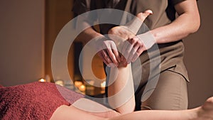 Professional physiotherapist male masseur in an office with cozy dark lighting makes a wellness foot massage to a female