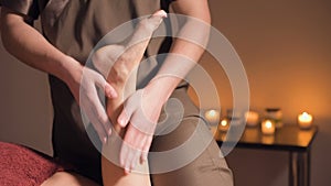 Professional physiotherapist male masseur in an office with cozy dark lighting makes a wellness foot massage to a female