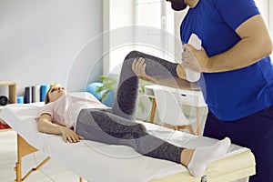 Professional physiotherapist at modern clinic examining knee flexion of young woman