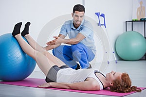 Professional physiotherapist and sportswoman on mat exercising with ball