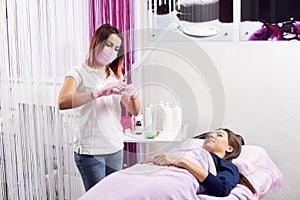 Professional in pink mask and gloves getting ready a syringe to start a procedure to a young client of a beauty salon