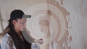 Professional plasterer female spackles the wall, applies and spreads plaster on a spatula in overalls and ball cap
