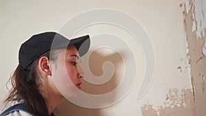 Professional plasterer female spackles the wall, applies and spreads plaster on a spatula in overalls and ball cap